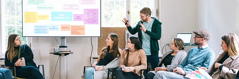 Skupina sedmi lidí v Impact Hubu diskutuje u projekce během workshopu.